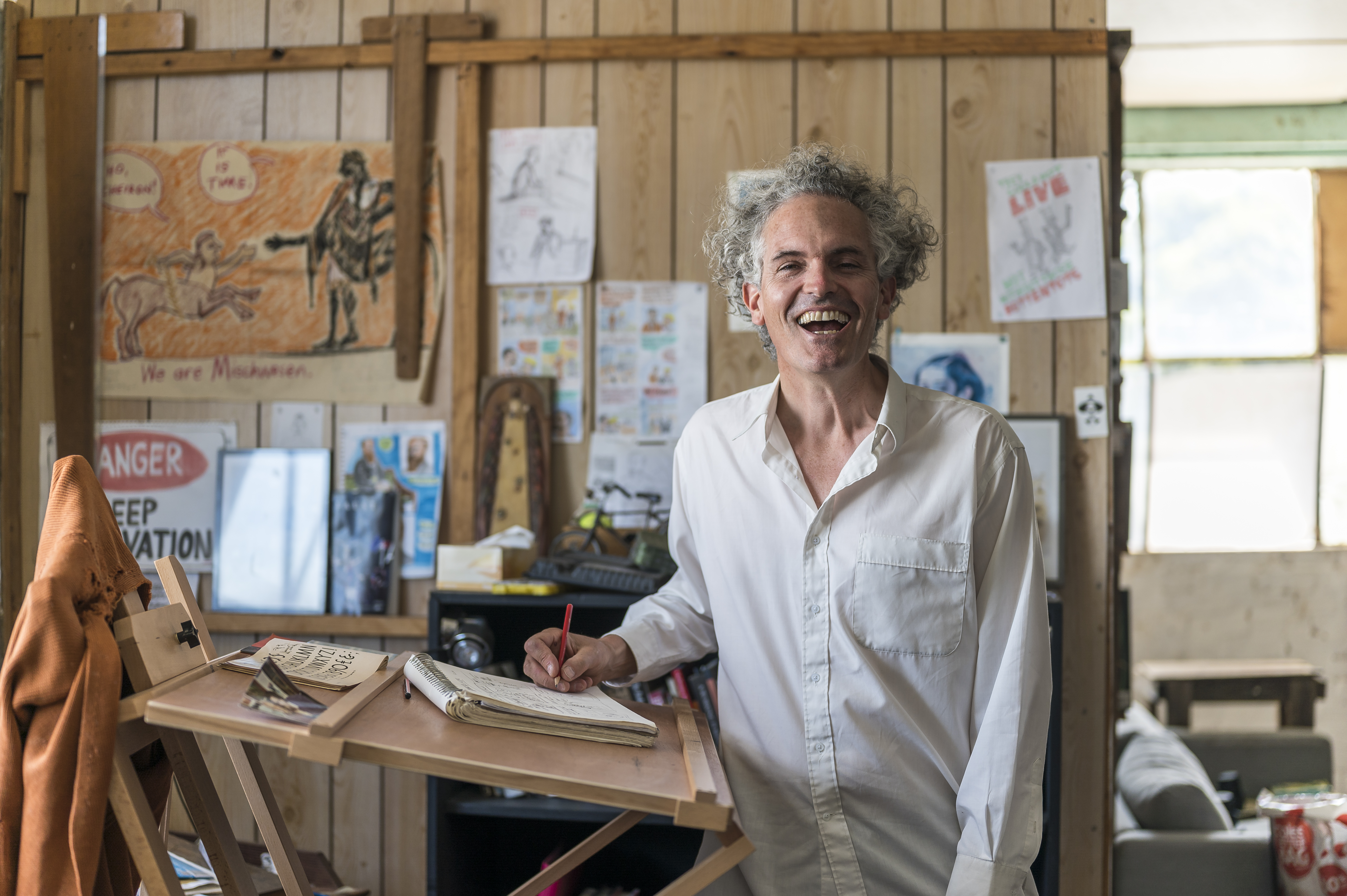 Bernard sitting on table in front of sketches with hands up