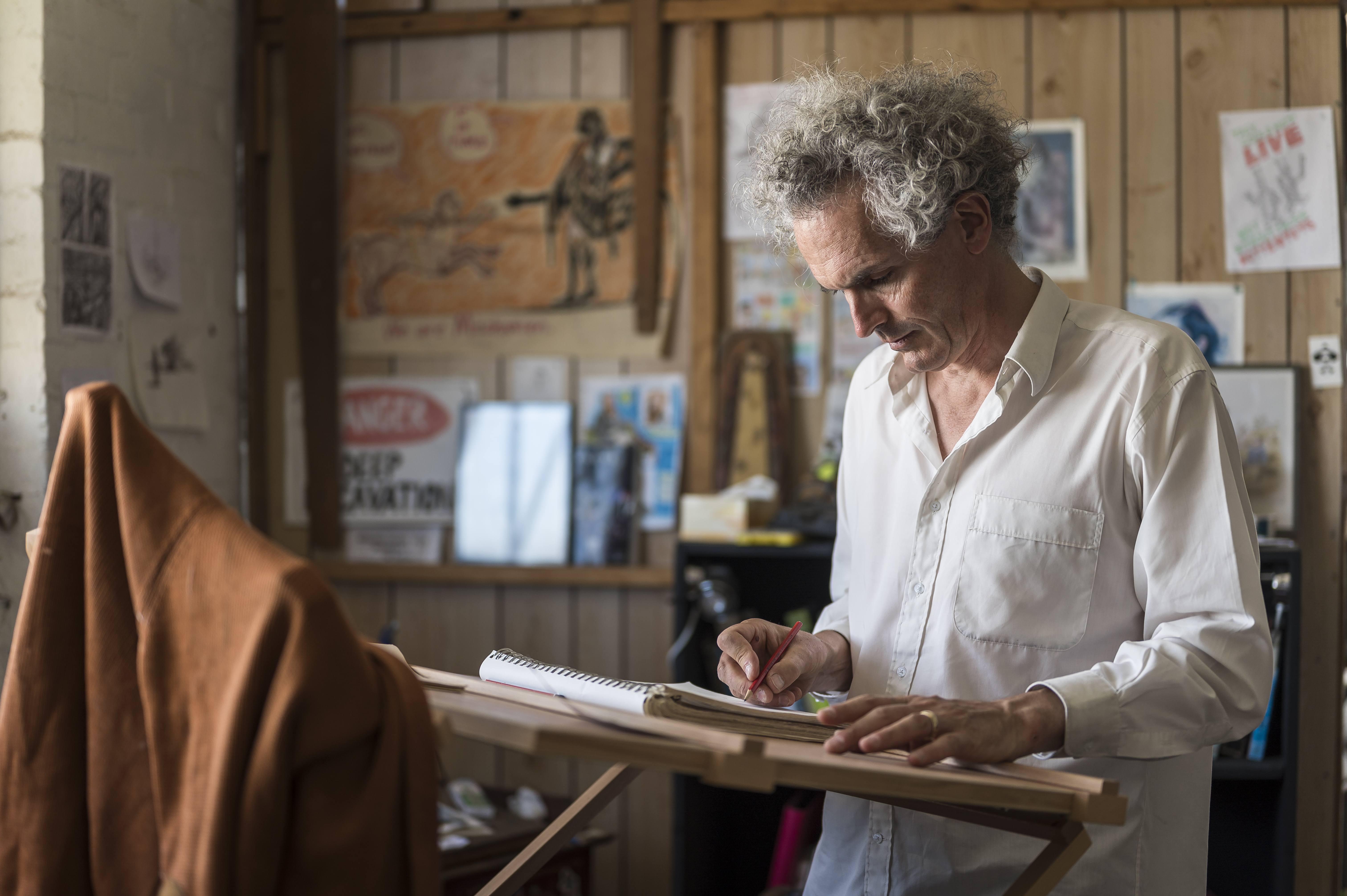 Bernard sitting on table in front of sketches with hands up